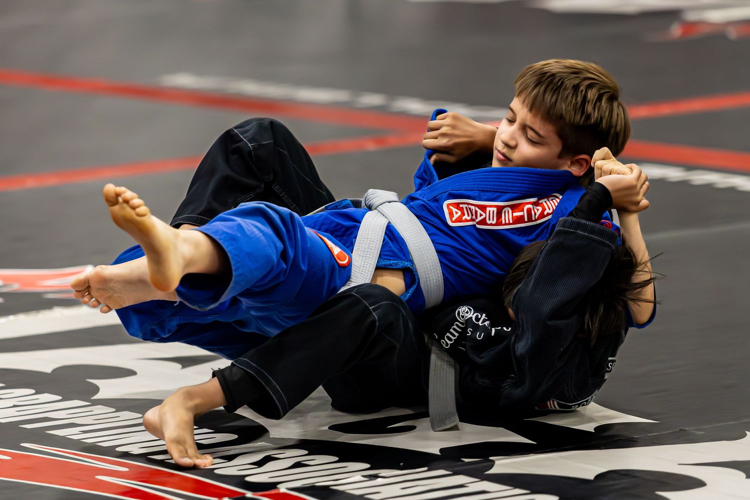 Two children sparring in Brazilian jiu-jitsu gi uniforms on a mat during a kids martial arts class.