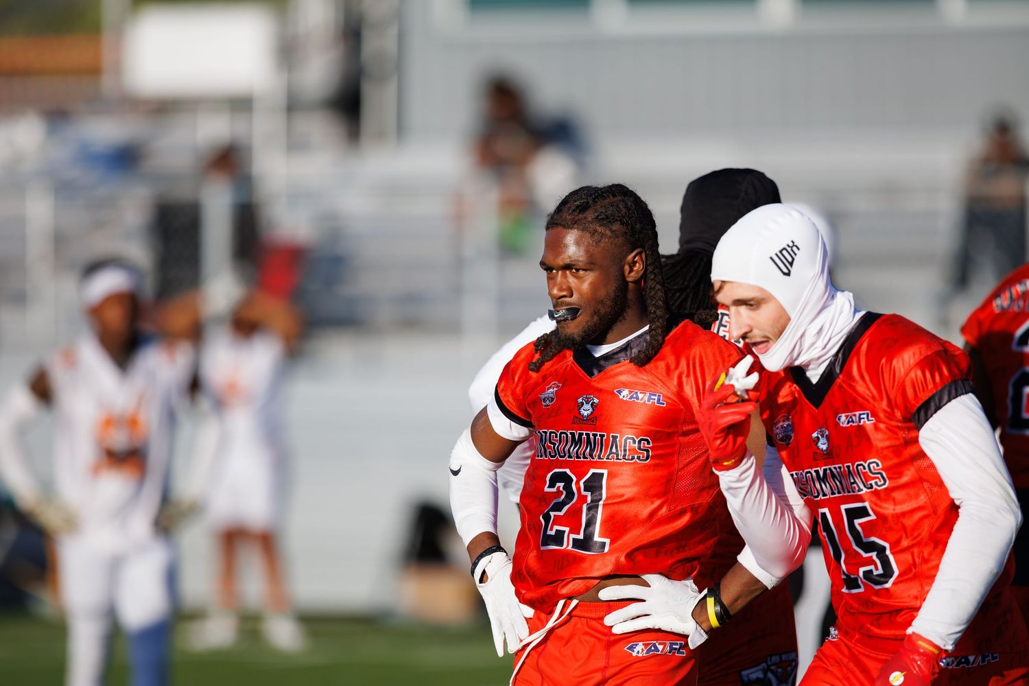 Two football players in red uniforms with numbers 21 and 15 stand on the sideline during a game.