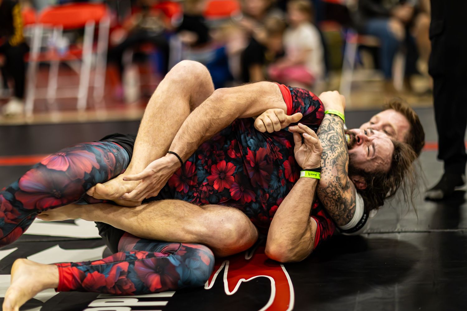 Two athletes compete in a grappling match on the mat during a Brazilian jiu-jitsu tournament.