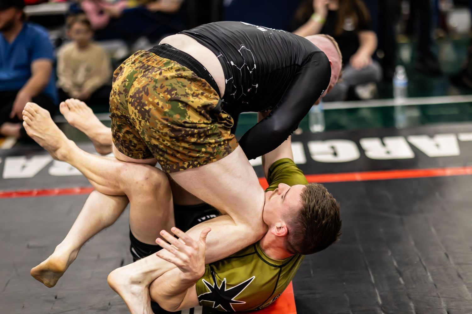 Two wrestlers compete on a mat, one pinning the other during an intense wrestling match at an indoor tournament.
