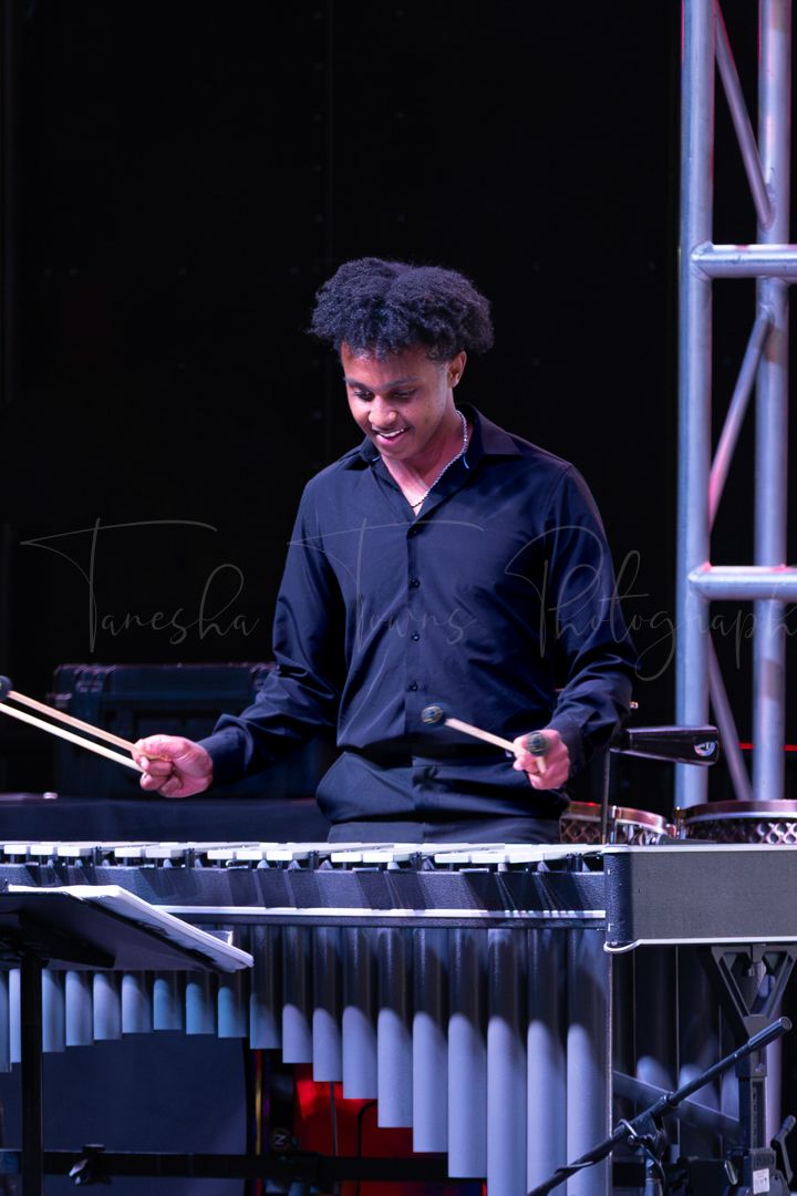 Musician playing vibraphone on dark stage with dramatic lighting.