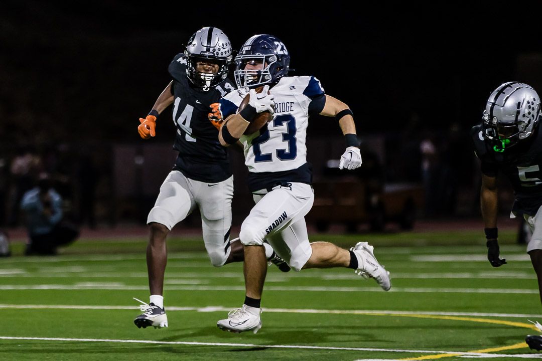 Football players battle for position during a ground play under stadium lights.