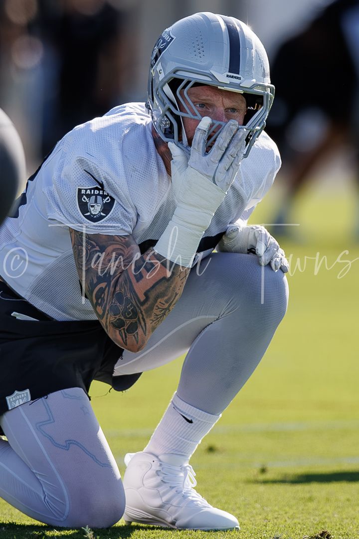 Raiders player kneeling on field in white uniform and helmet during NFL practice session.