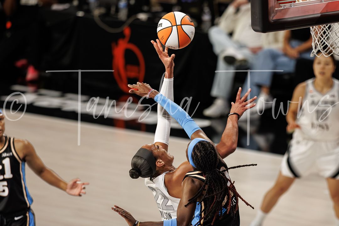 Two WNBA players battle for a rebound during an intense basketball game, with one player elevating for the ball.