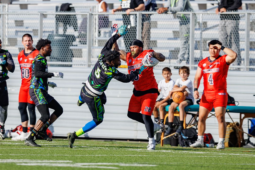 Football players in red and green uniforms compete for a pass during an intense outdoor game.