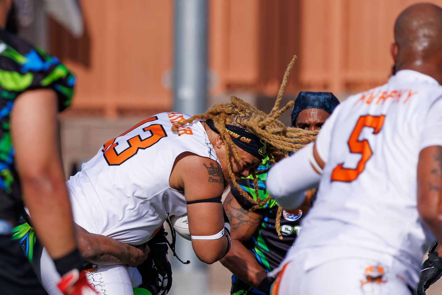 Football players in orange jerseys collide during an intense tackle in a competitive outdoor game.