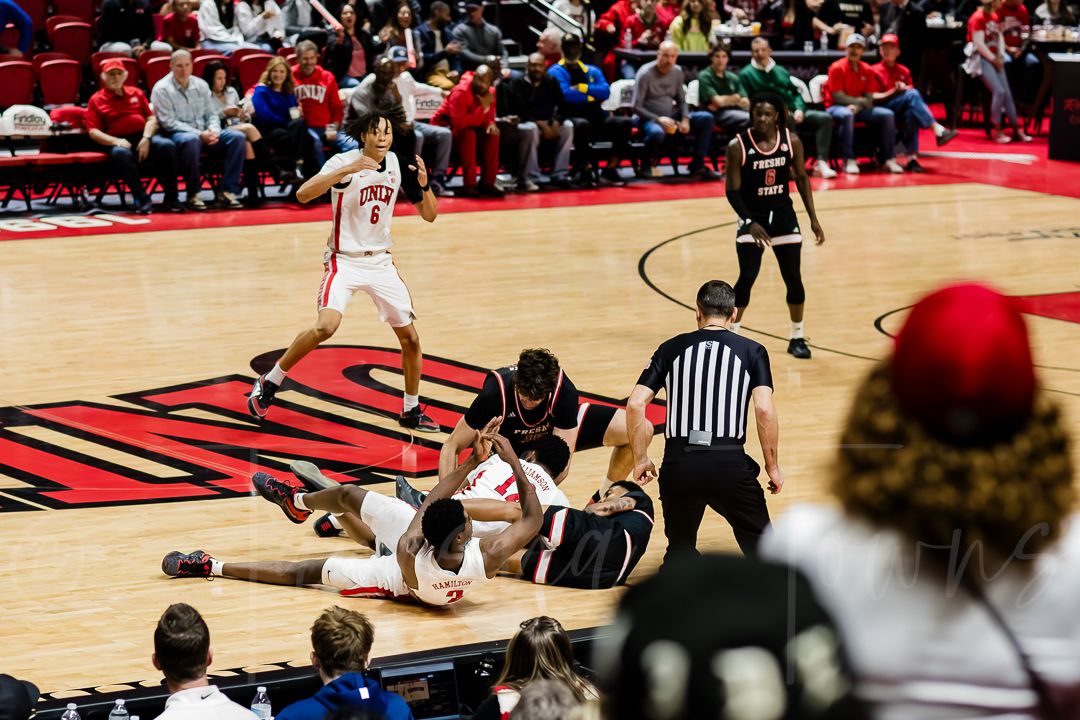 Wide view of a basketball court during gameplay with spectators in red seats.
