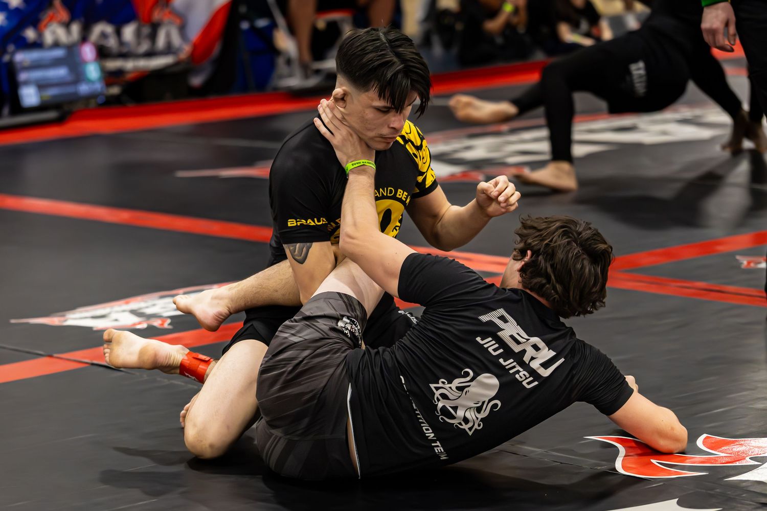 Two competitors grappling on a black mat during a jiu-jitsu tournament, one wearing a Peru BJJ uniform.
