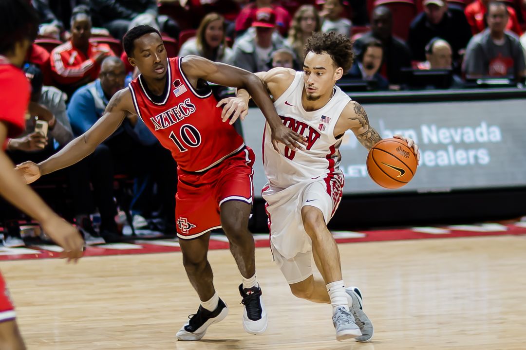 Basketball players in red and white uniforms compete for possession during an intense college game at Nevada.