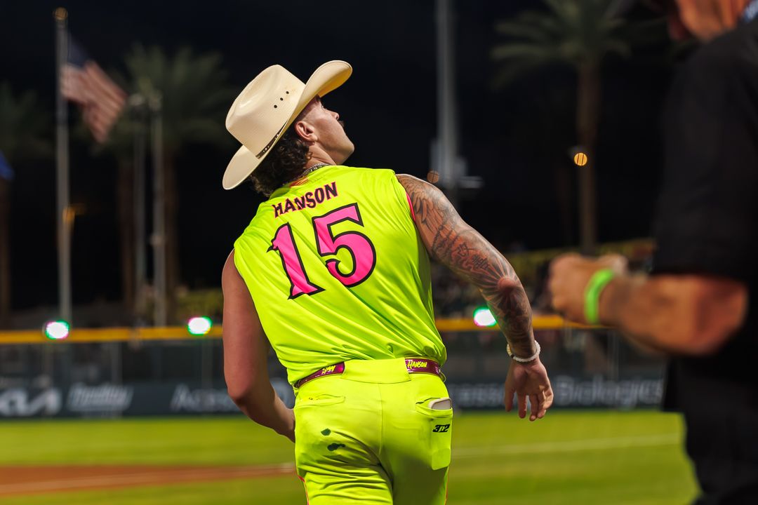 Player #15 Hanson in neon yellow jersey and cowboy hat on baseball field at night.
