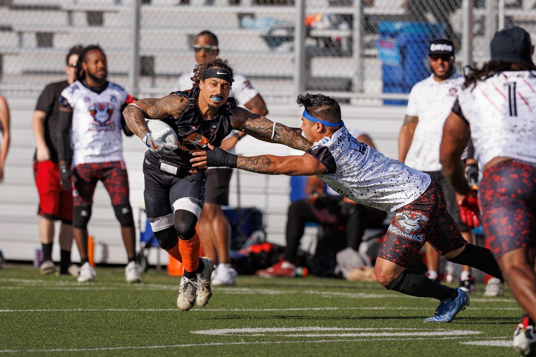 Rugby players compete on a field, with a tattooed athlete evading a tackle during an intense outdoor match.