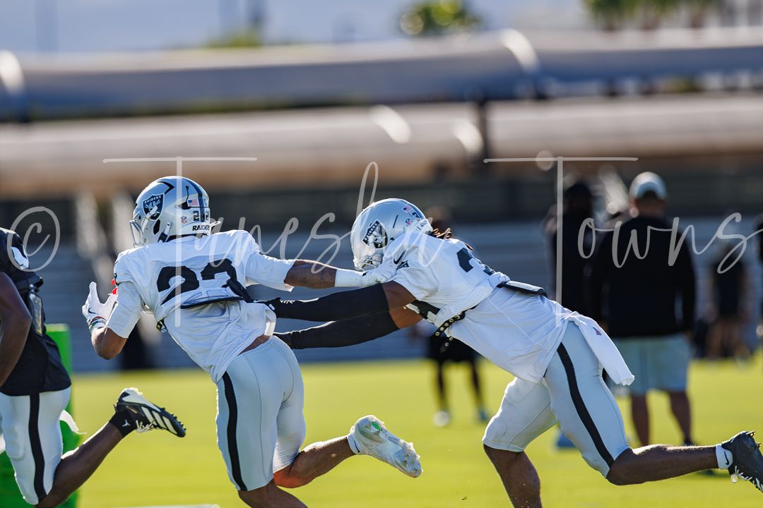 Two Raiders football players practice blocking drills on a sunny training camp field.