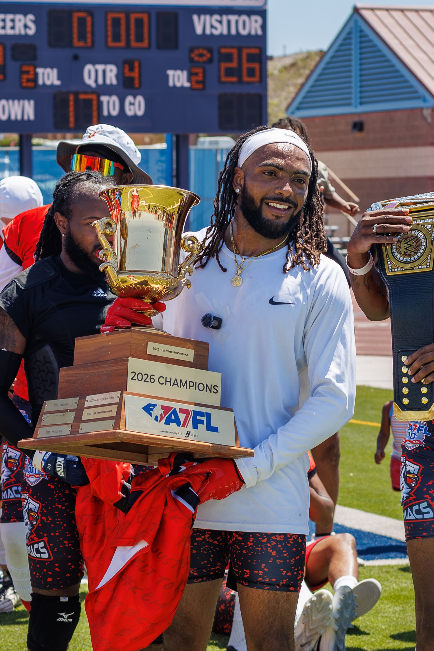 Athlete proudly holds 2026 AAFL Champions trophy on football field after championship victory.