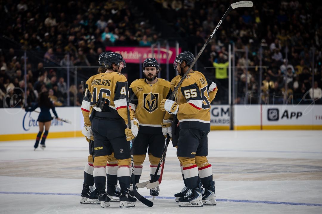 NHL hockey players in gold jerseys gather on the ice during a game at T-Mobile Arena.