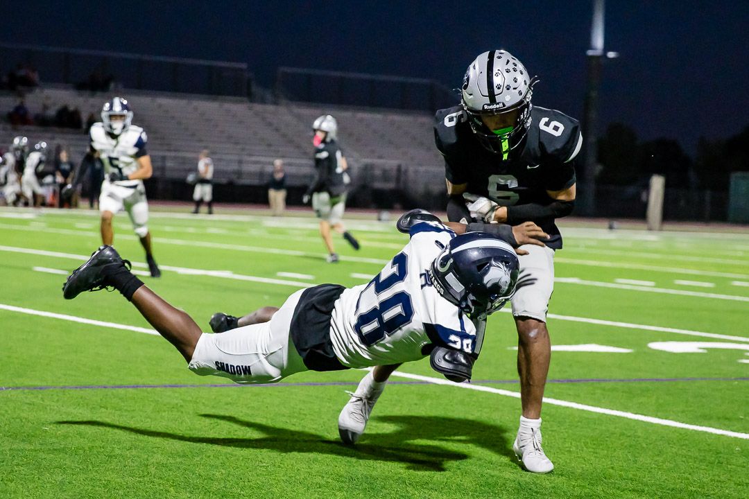 Football players diving and tackling during intense nighttime game action.