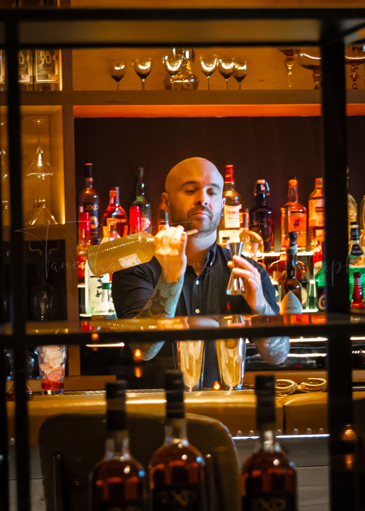 Bartender mixing drinks behind a well-stocked bar with colorful bottle displays.