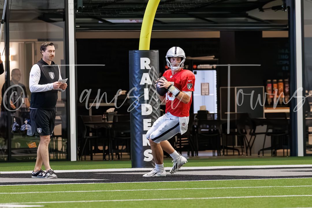 Raiders quarterback runs drills near team logo pillar during practice.