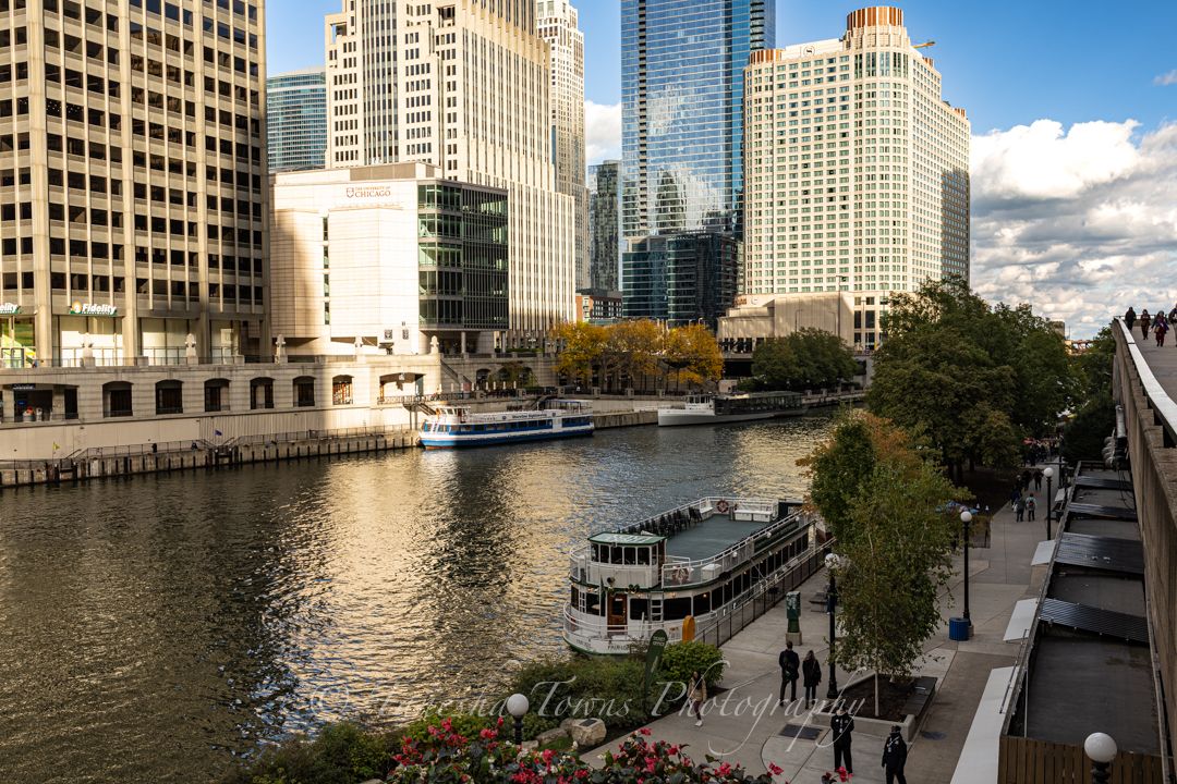 Modern skyscrapers line the Chicago River on a sunny day as boats cruise along the waterfront in downtown Chicago.