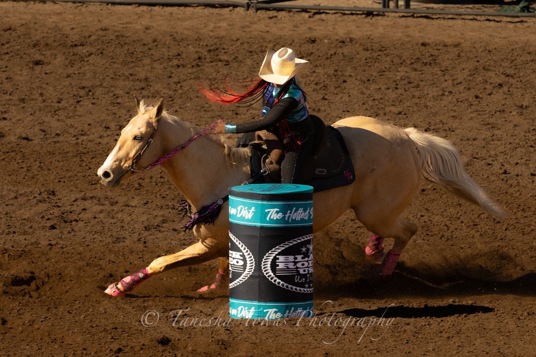 A palomino horse and rider compete in a barrel racing event at a rodeo arena.