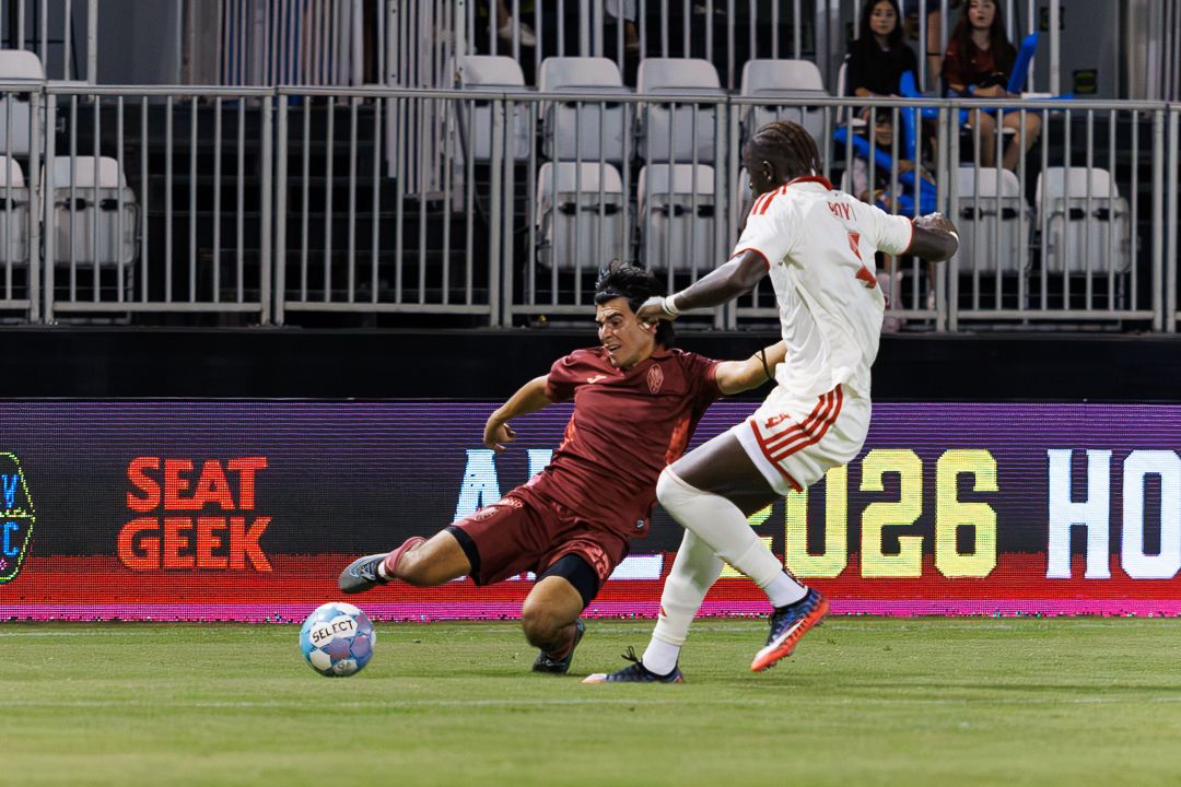 Soccer player executes a sliding tackle on opponent during competitive MLS match on professional turf.