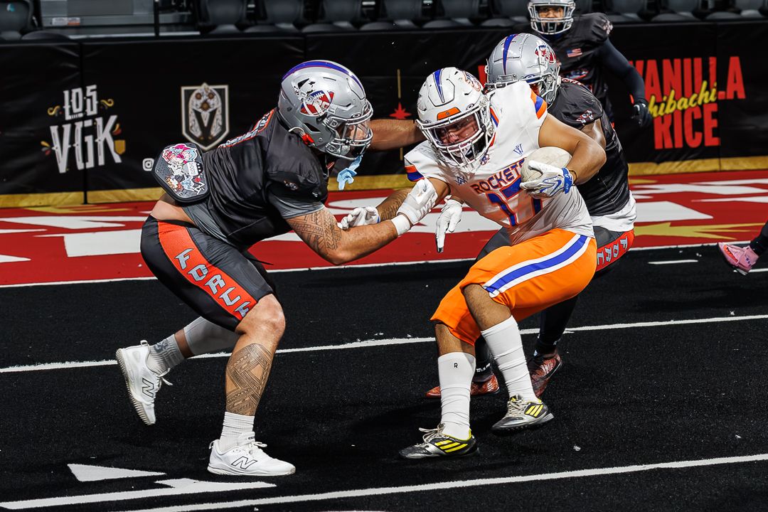Indoor football game action shot with players in orange and black uniforms competing near the end zone.