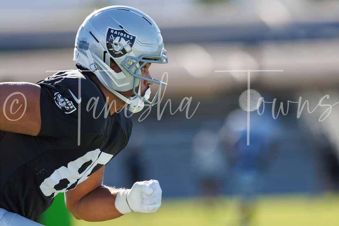 Las Vegas Raiders player in silver helmet celebrates during NFL training camp practice on sunny day.