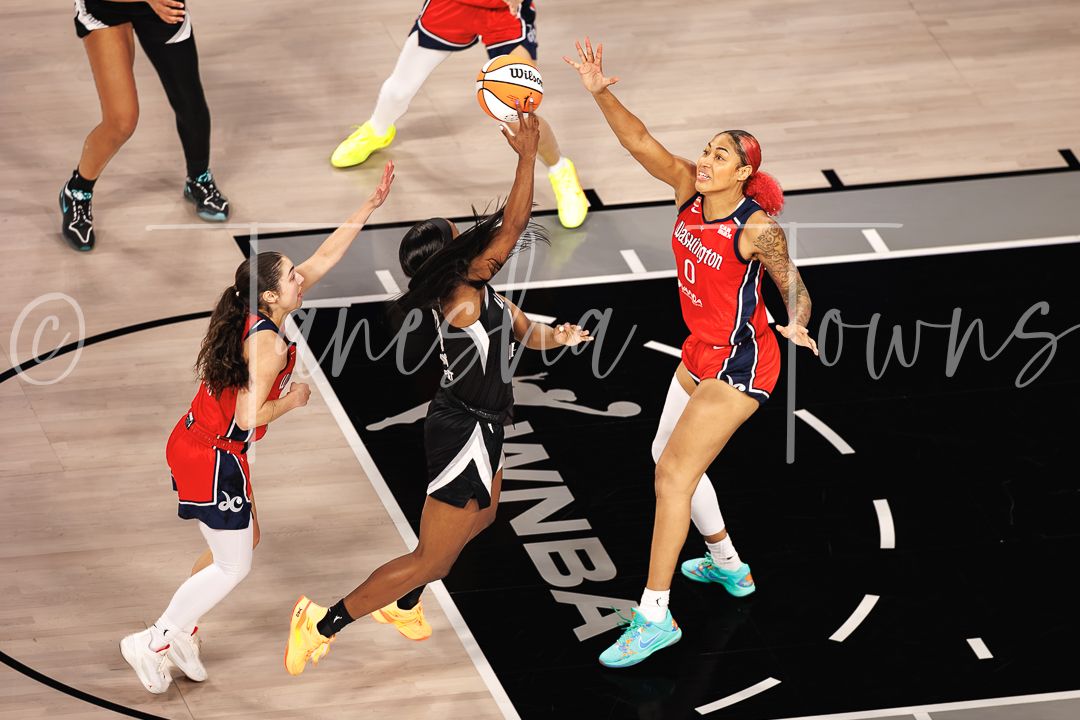 WNBA player drives to the basket against defenders in red uniforms during a professional basketball game.