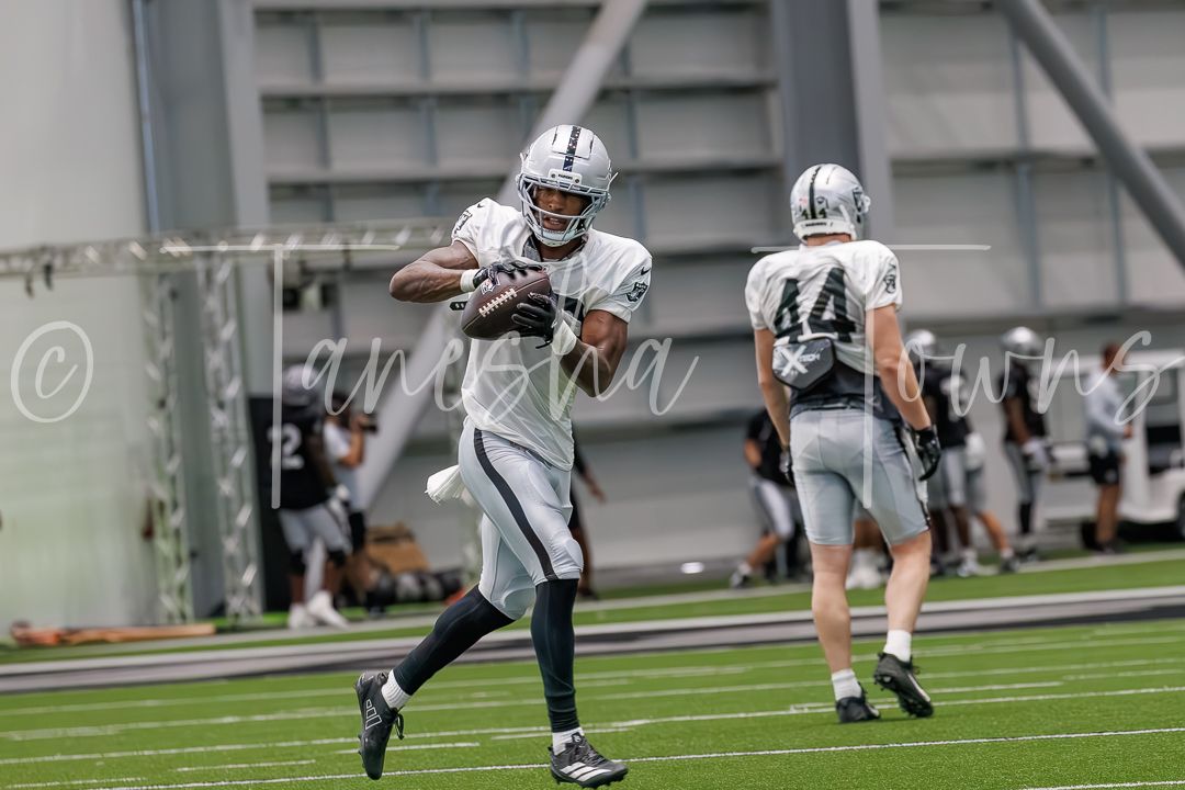 Football players in black and white uniforms practice drills on an indoor field during team training.