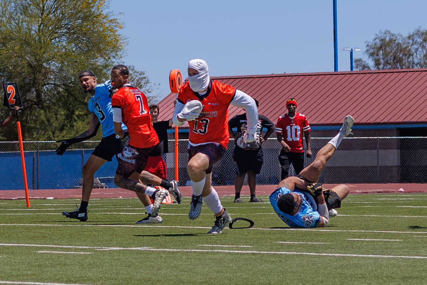 Flag football players compete on a sunny field, with one player running with the ball while another dives to make a stop.