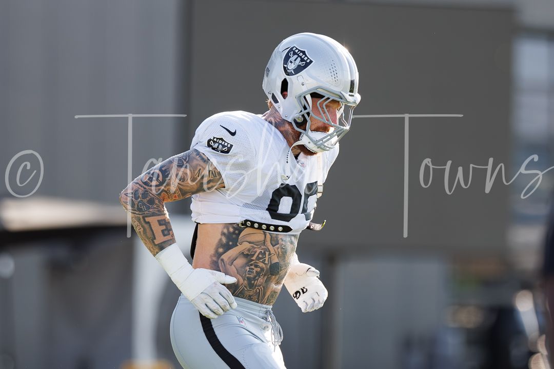Tattooed Raiders wide receiver in white uniform sprints during NFL training camp practice.