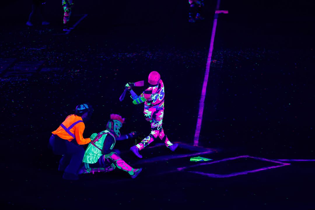People playing glow-in-the-dark mini golf under black lights at night, wearing neon fluorescent clothing.