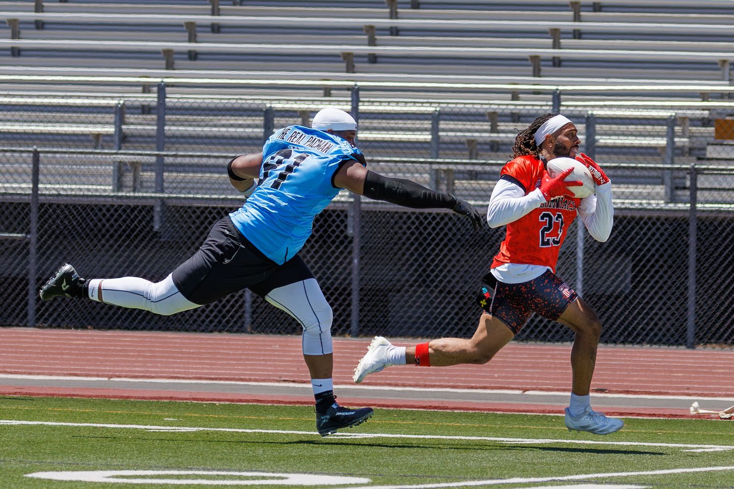 Two flag football players race downfield during an outdoor game on a sunny day.
