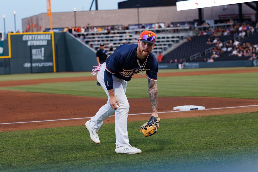 Baseball player in navy uniform fields a ball on the diamond during a professional game under stadium lights.