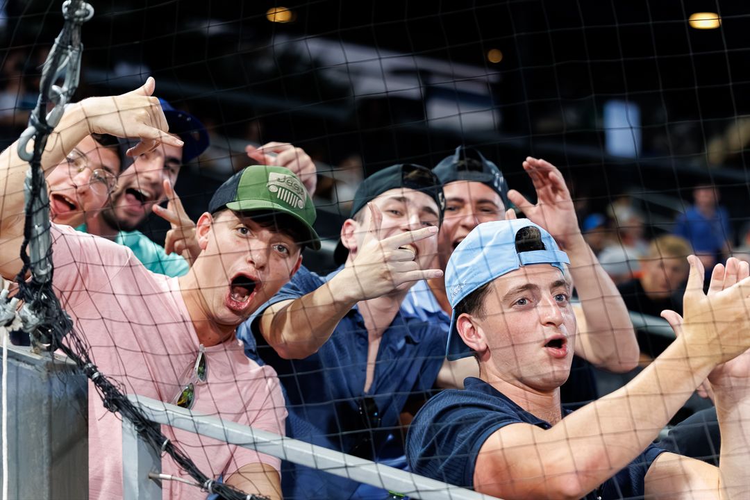 Excited baseball fans cheer behind a net at a stadium.
