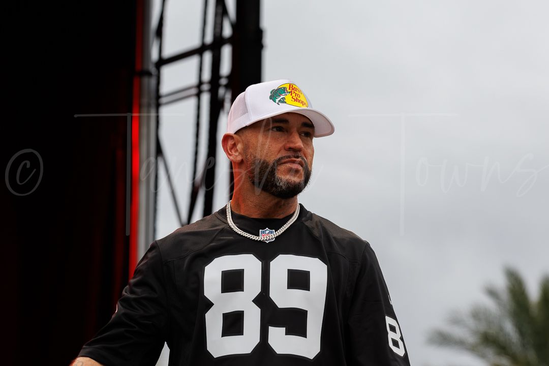 Male performer in Raiders jersey 89 and white cap on outdoor festival stage.