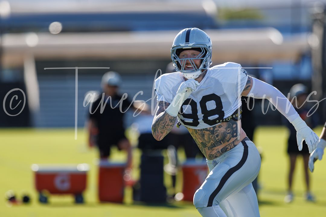 Raiders player #98 runs a drill during NFL training camp practice on a sunny day.