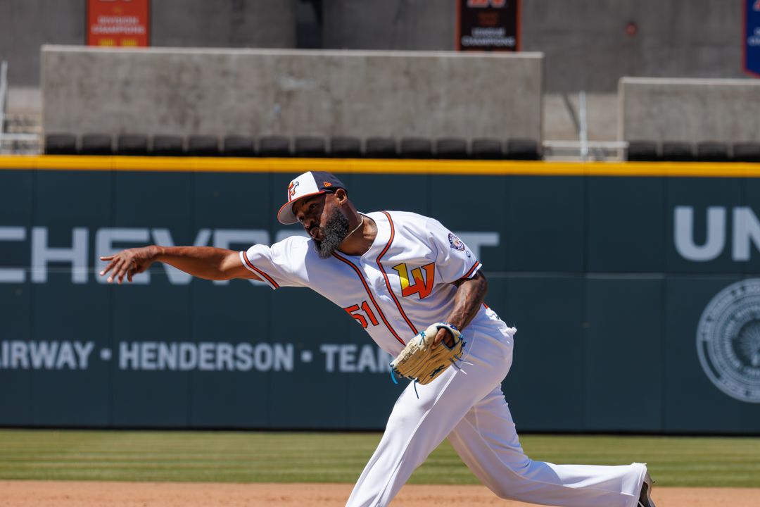 Baseball infielder in white uniform makes a strong throwing motion on the diamond during a sunny afternoon game.