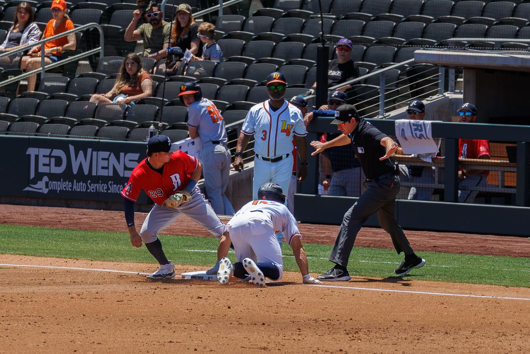 Baseball player sliding into base as fielder applies tag with umpire signaling during game.