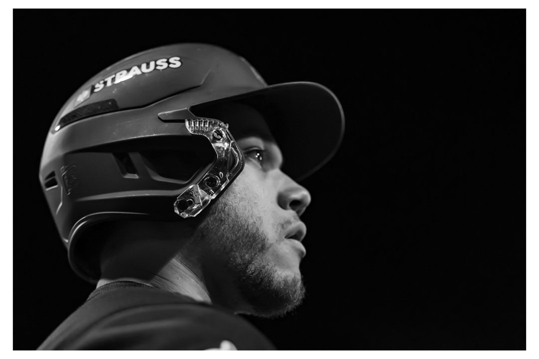 Black and white profile portrait of a baseball player wearing a Strauss batting helmet with chin guard.