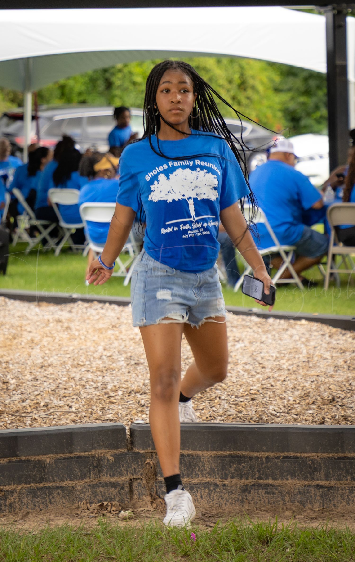 People in blue family reunion shirts walking on wood chips under a covered area.