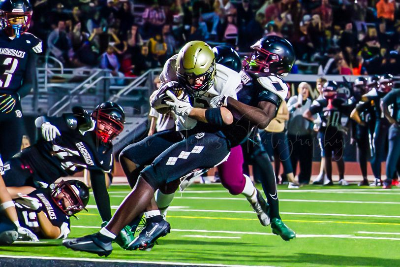 Two football teams clash in dramatic tackle during night game on artificial turf.
