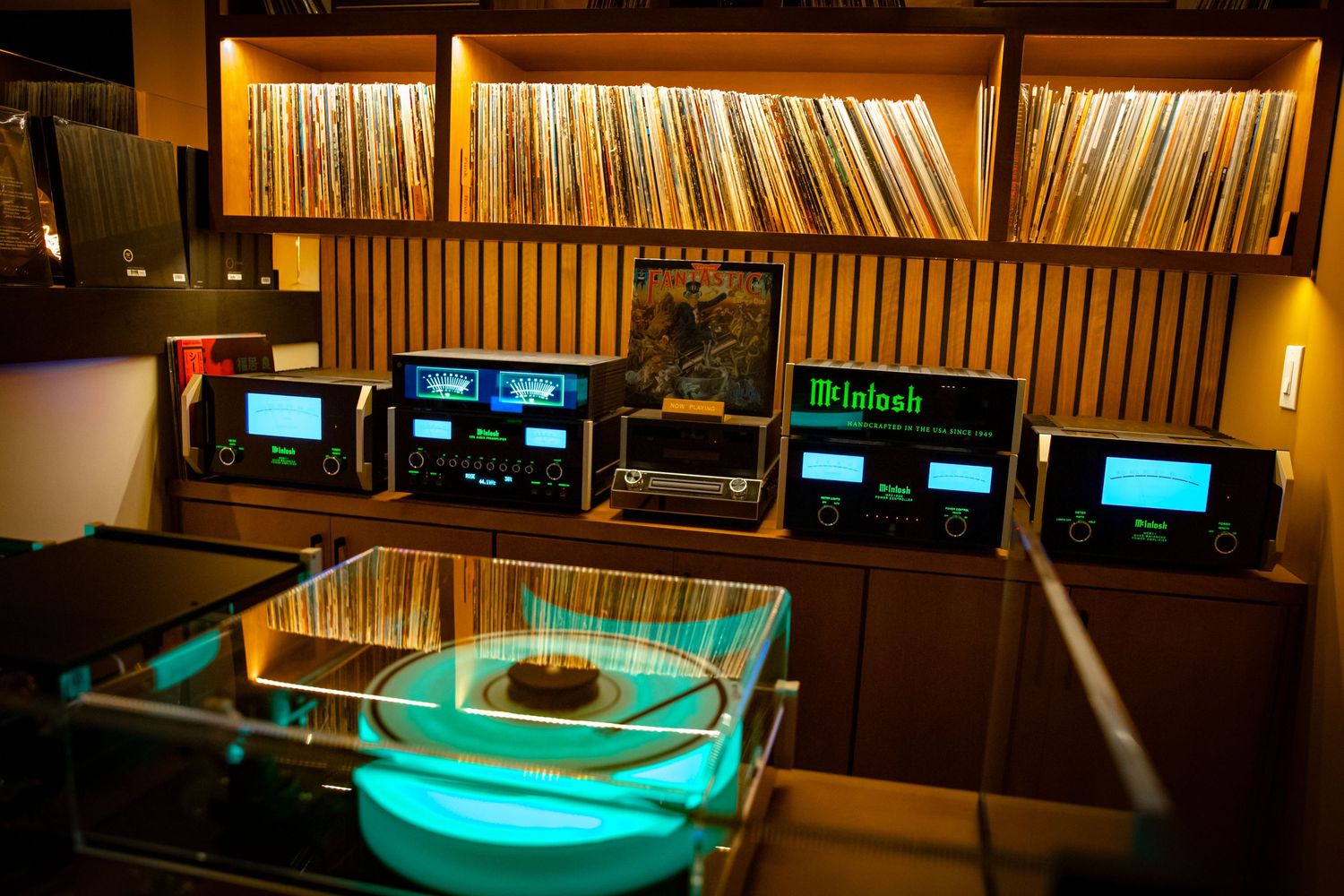 Modern recording studio interior with illuminated turntables and extensive vinyl record collection on shelves.