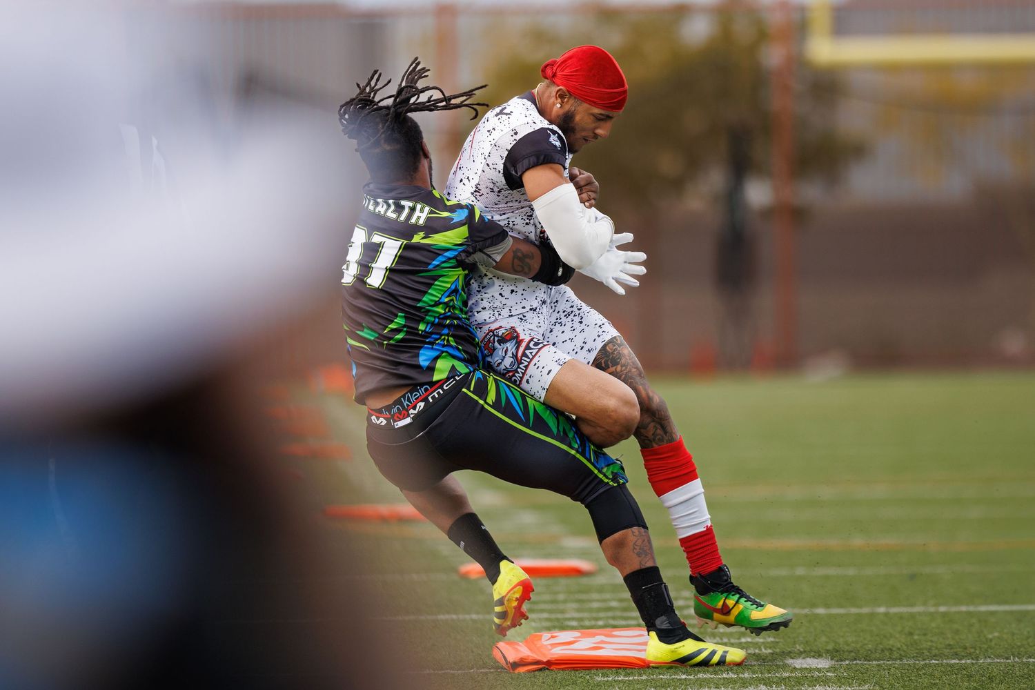 Two flag football players compete on a turf field, one in a black stealth jersey #17 being blocked by an opponent.