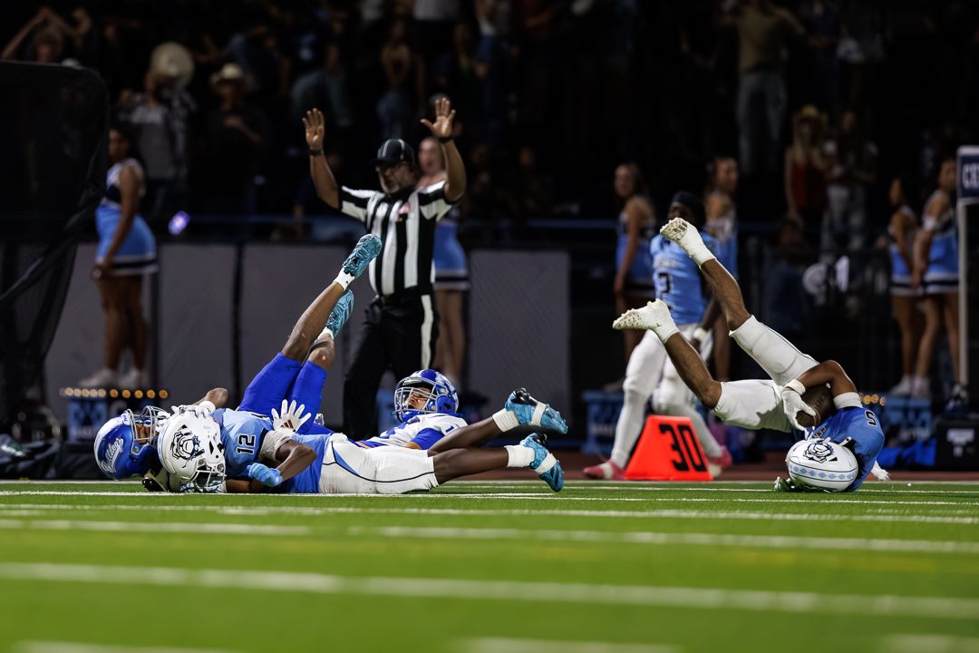 Football players collide on the field during a night game as a referee signals overhead.