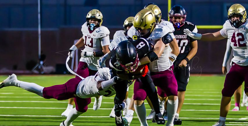 Football players tackle opponent during intense gameplay on illuminated field.
