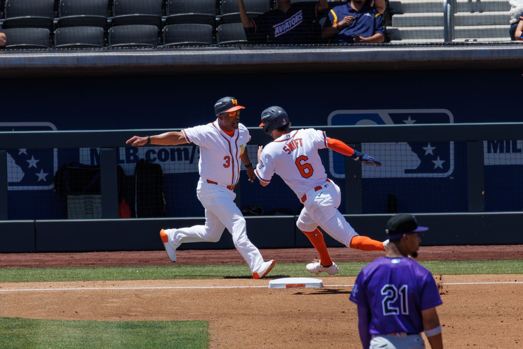Two baseball players in orange uniforms run bases during daytime MLB game at modern ballpark.