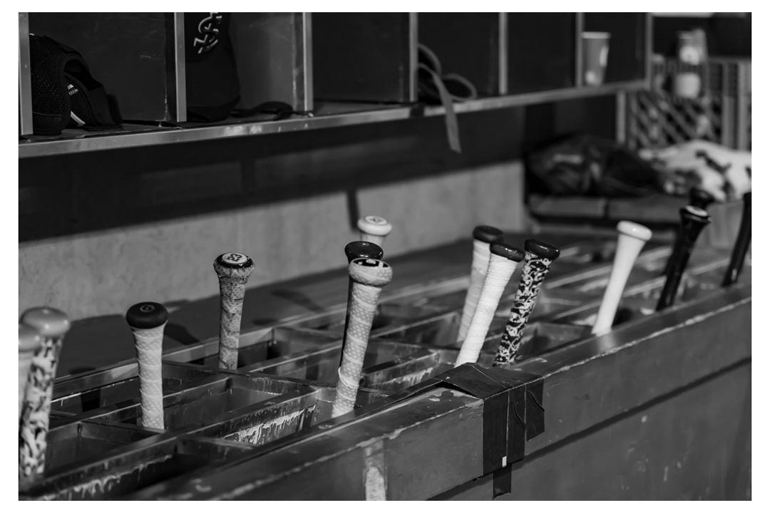 Black and white photo of baseball bats stored in a dugout bat rack during a game.
