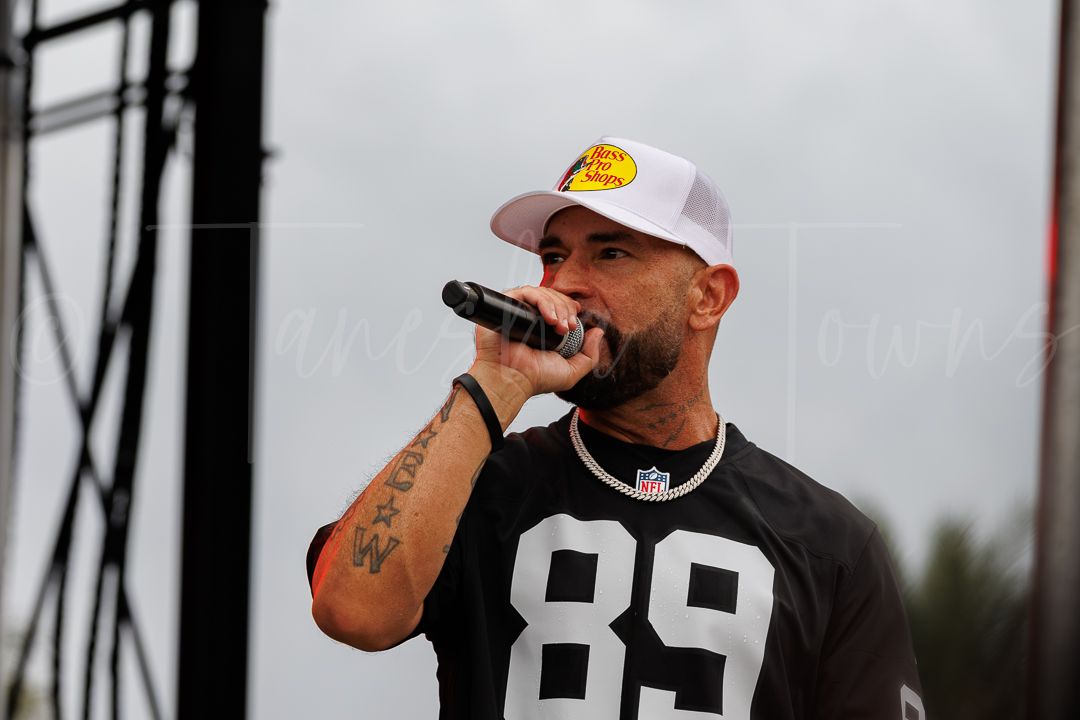 Man in white cap and NFL jersey 89 performs on outdoor stage holding microphone with tattoos visible.
