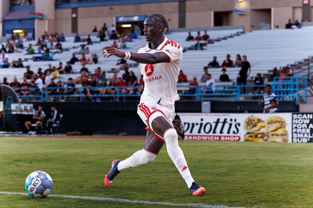 Soccer player in white uniform dribbling ball on field during a professional match at a stadium.