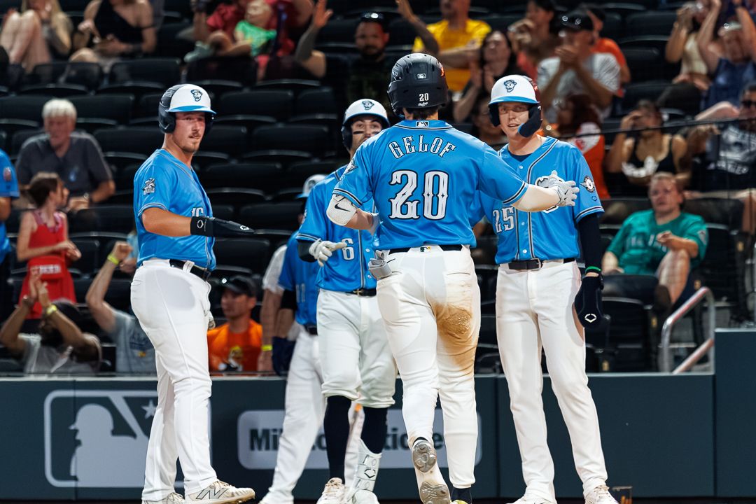 Baseball players in teal uniforms celebrate on field, player #20 Bellue greeted by teammates after scoring a run.